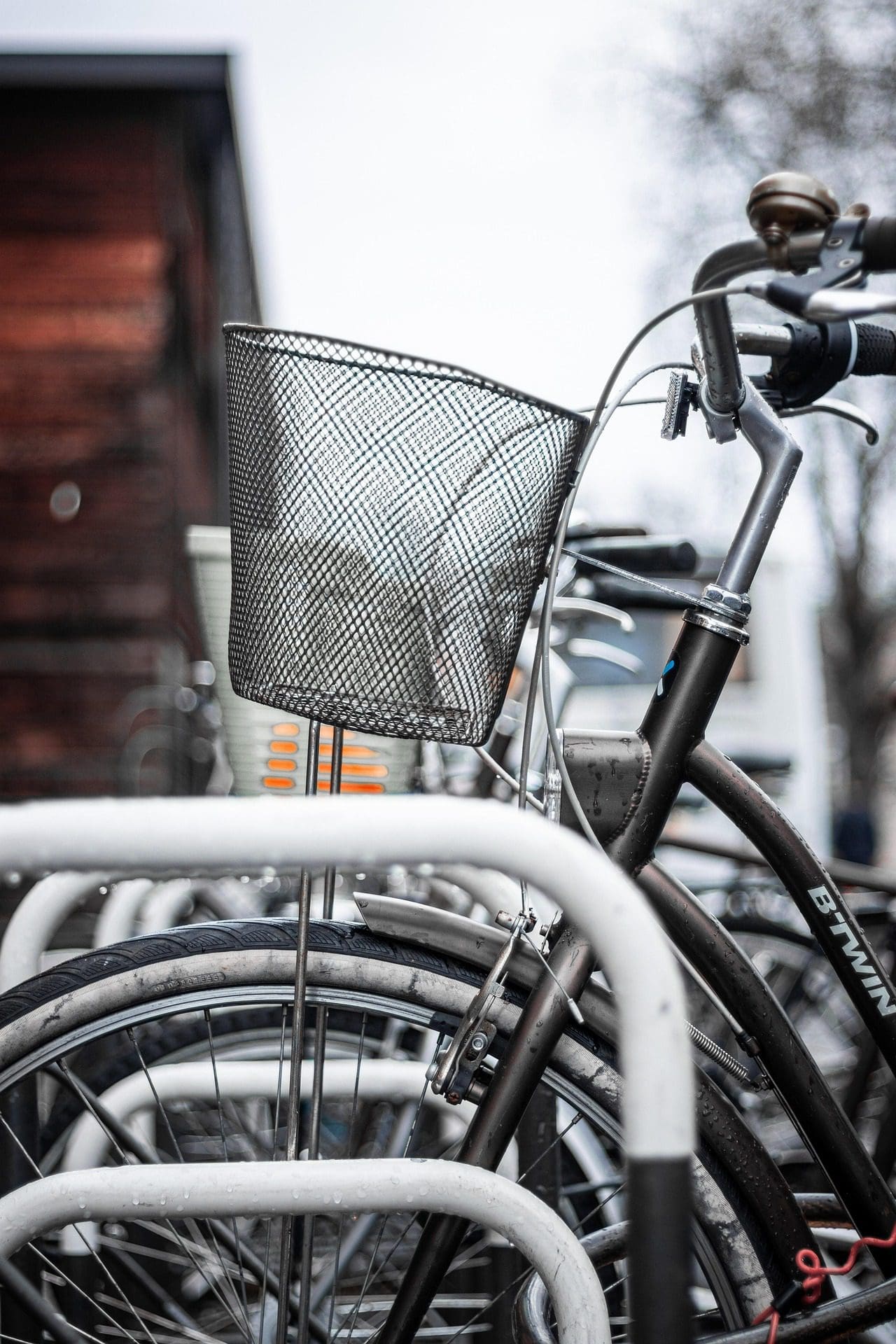 Gros plan d'une bicyclette garée sur un support à vélos. L'accent est mis sur le panier métallique avant, plusieurs autres vélos étant visibles à l'arrière-plan. L'image montre un environnement extérieur nuageux, mettant l'accent sur le cyclisme urbain.