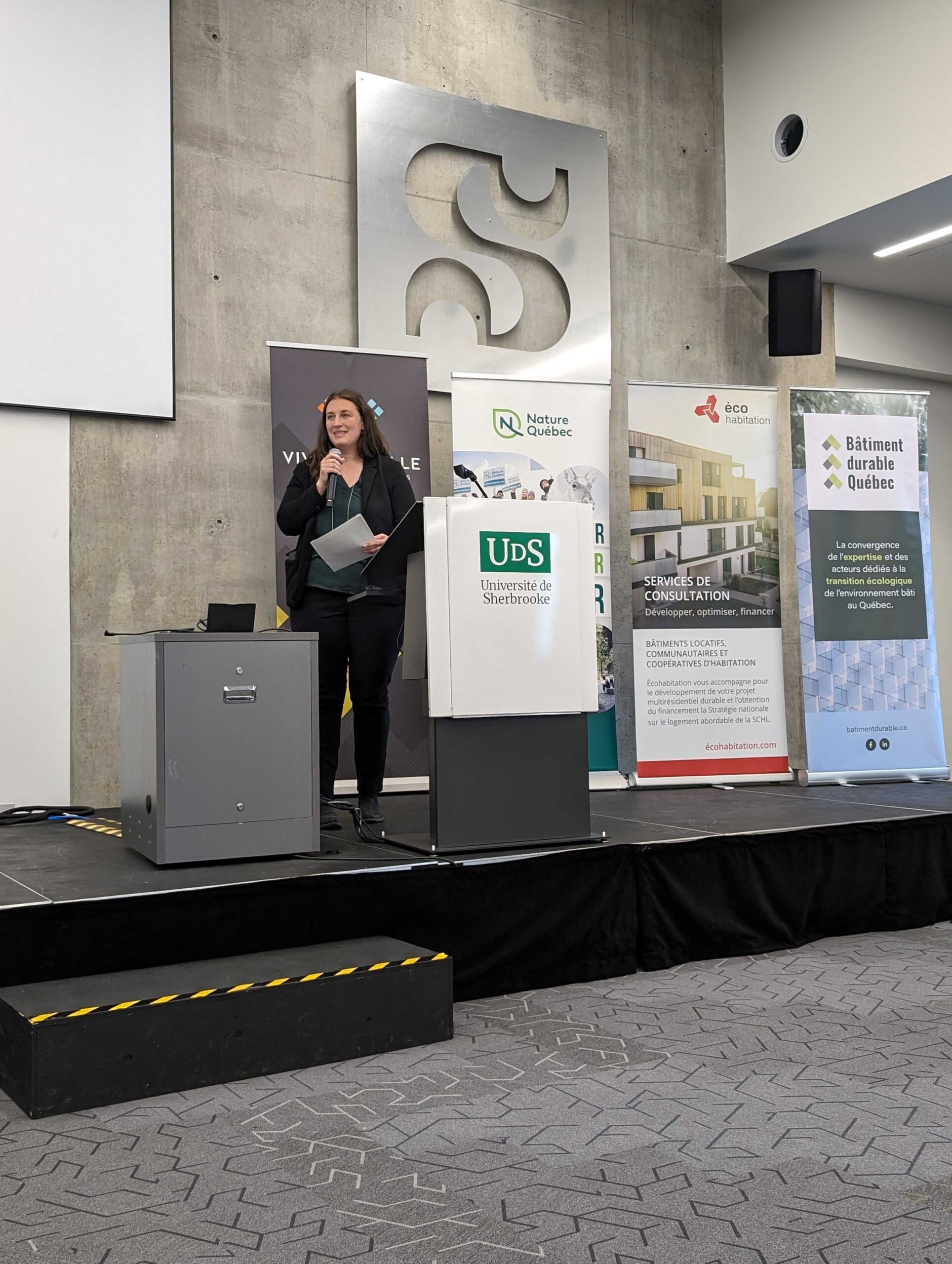 Une grande salle de conférence bourdonne d'impatience lorsque les participants se rassemblent pour le symposium sur les bâtiments sans carbone. Assis face à un panel de quatre orateurs, ils écoutent attentivement une présentation sur l'urbanisme affichée à l'écran, certains prenant des notes ou des photos.