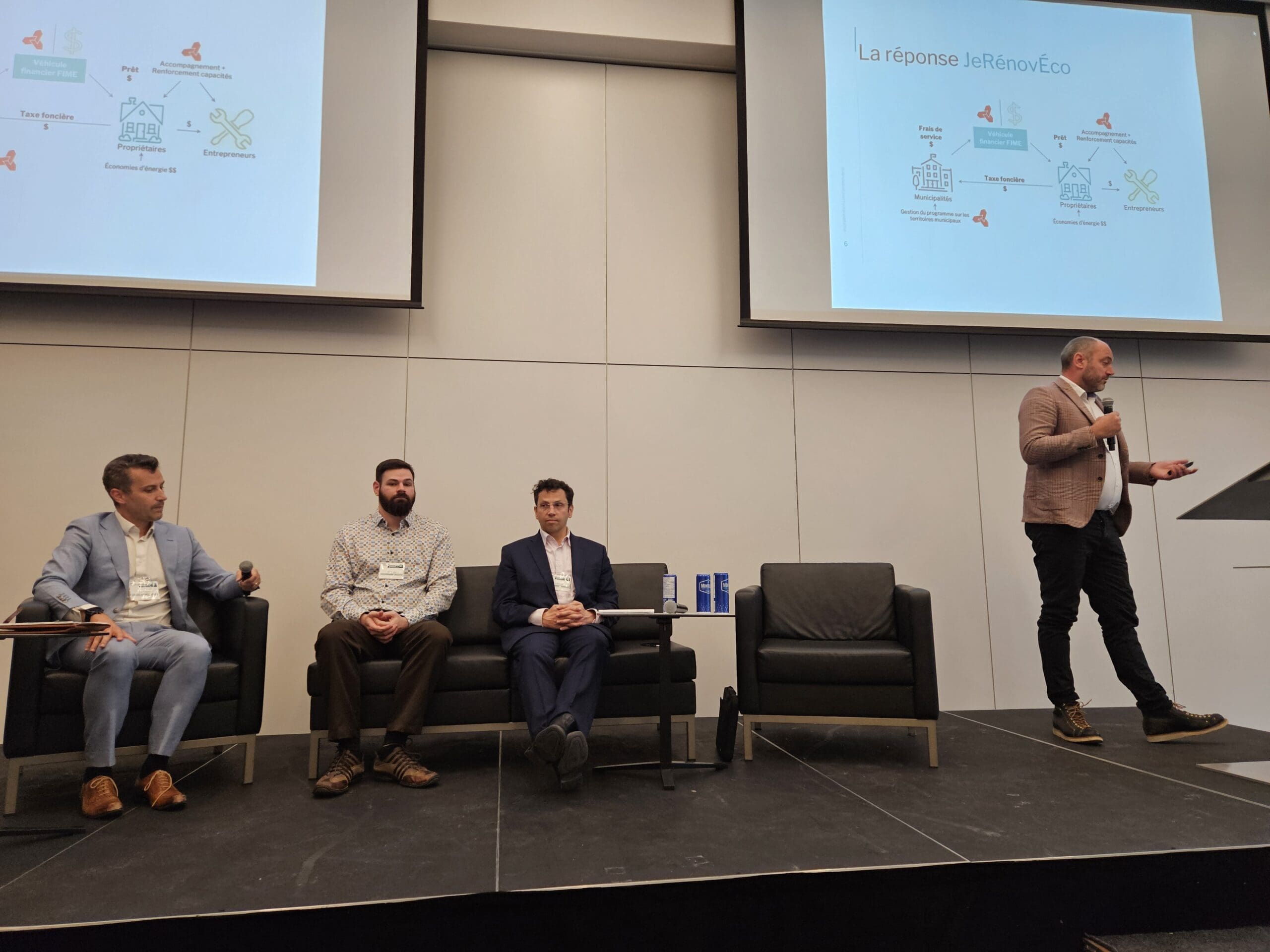 Un homme se tient sur un podium et s'adresse à un public lors d'un événement organisé par Nature Québec. Trois hommes sont assis sur la scène, face au public, alors qu'une diapositive de présentation sur JeRénovEco, remplie de textes et de diagrammes, apparaît au-dessus d'eux.