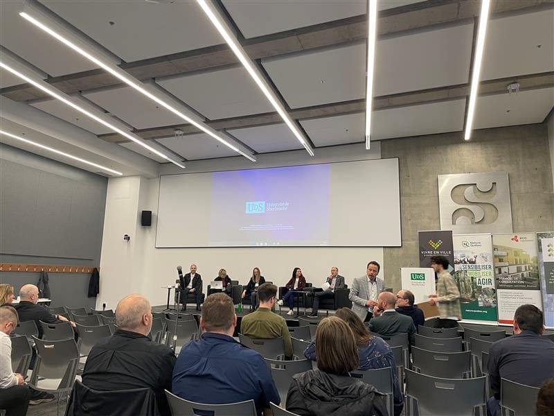 Une table ronde est en cours dans une salle de conférence moderne où six personnes sont assises sur la scène. Accueillis par Nature Québec, les participants sont assis en rangs, écoutant et discutant avec les panélistes. De grands écrans de présentation et des bannières sont affichés en arrière-plan.