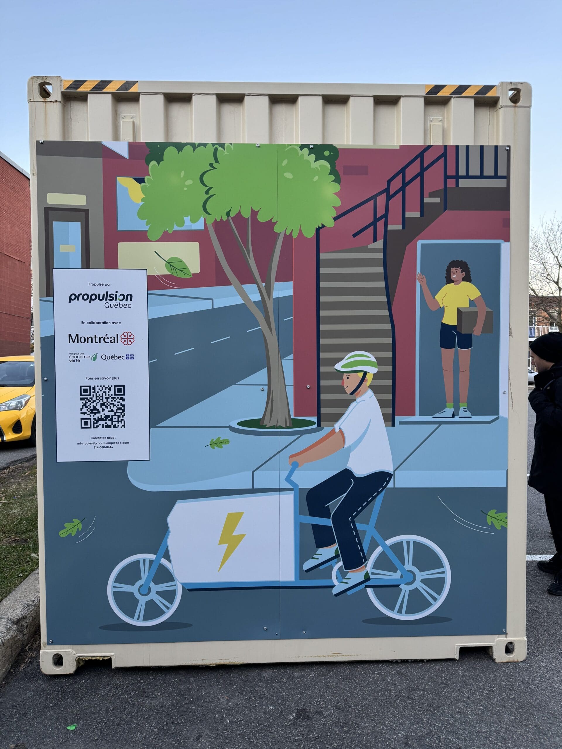 Une murale sur un conteneur, réalisée par Propulsion Québec, représente un cycliste casqué qui se déplace à vélo électrique dans les rues de la ville. En arrière-plan, un arbre et un trottoir apparaissent avec une personne se tenant à proximité. Un code QR et du texte sont visibles sur le côté gauche.