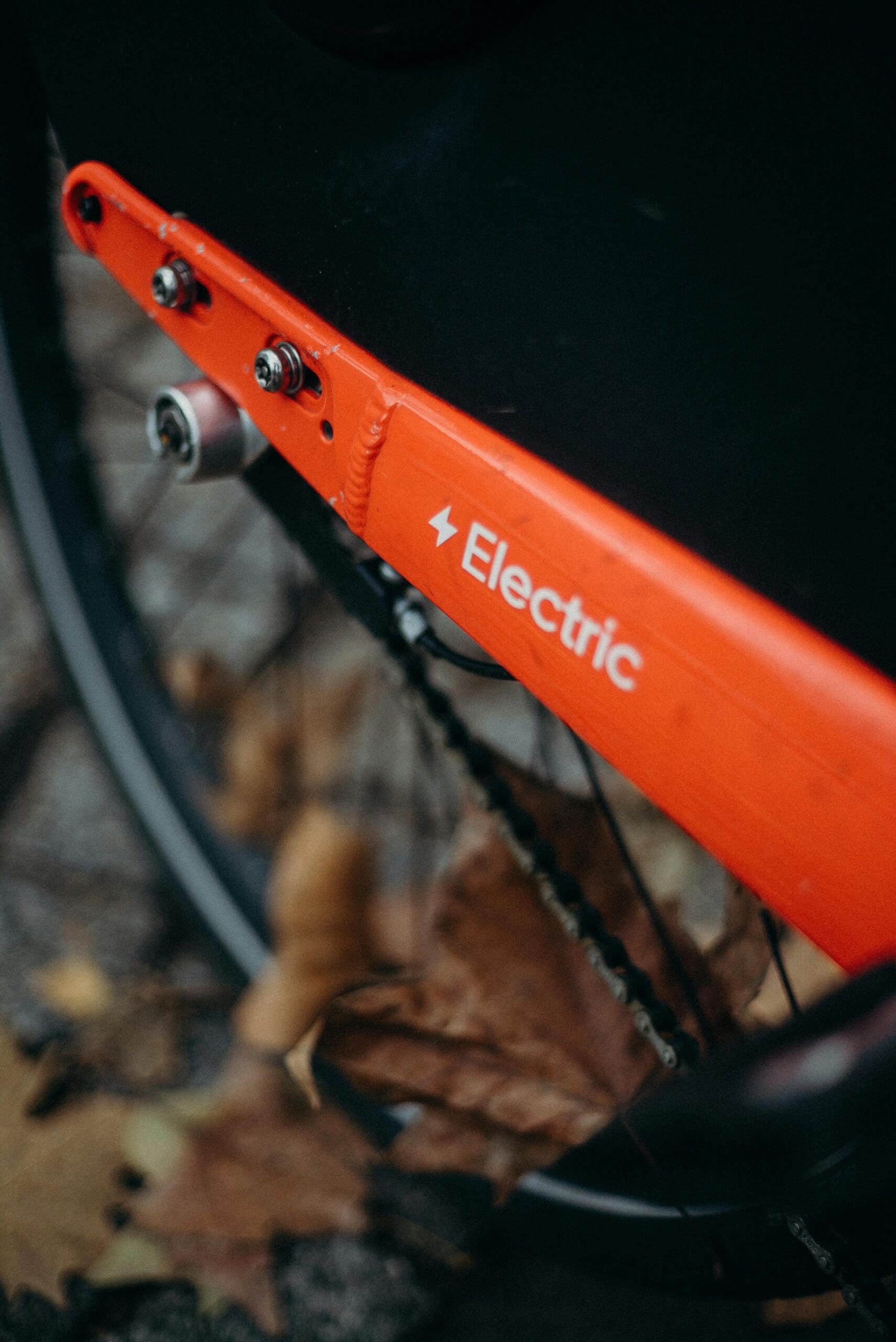 Gros plan de la partie arrière d'un vélo électrique, avec un cadre rouge portant le mot « Electric » et le symbole d'un éclair. L'arrière-plan montre des feuilles d'automne tombées sur le sol.