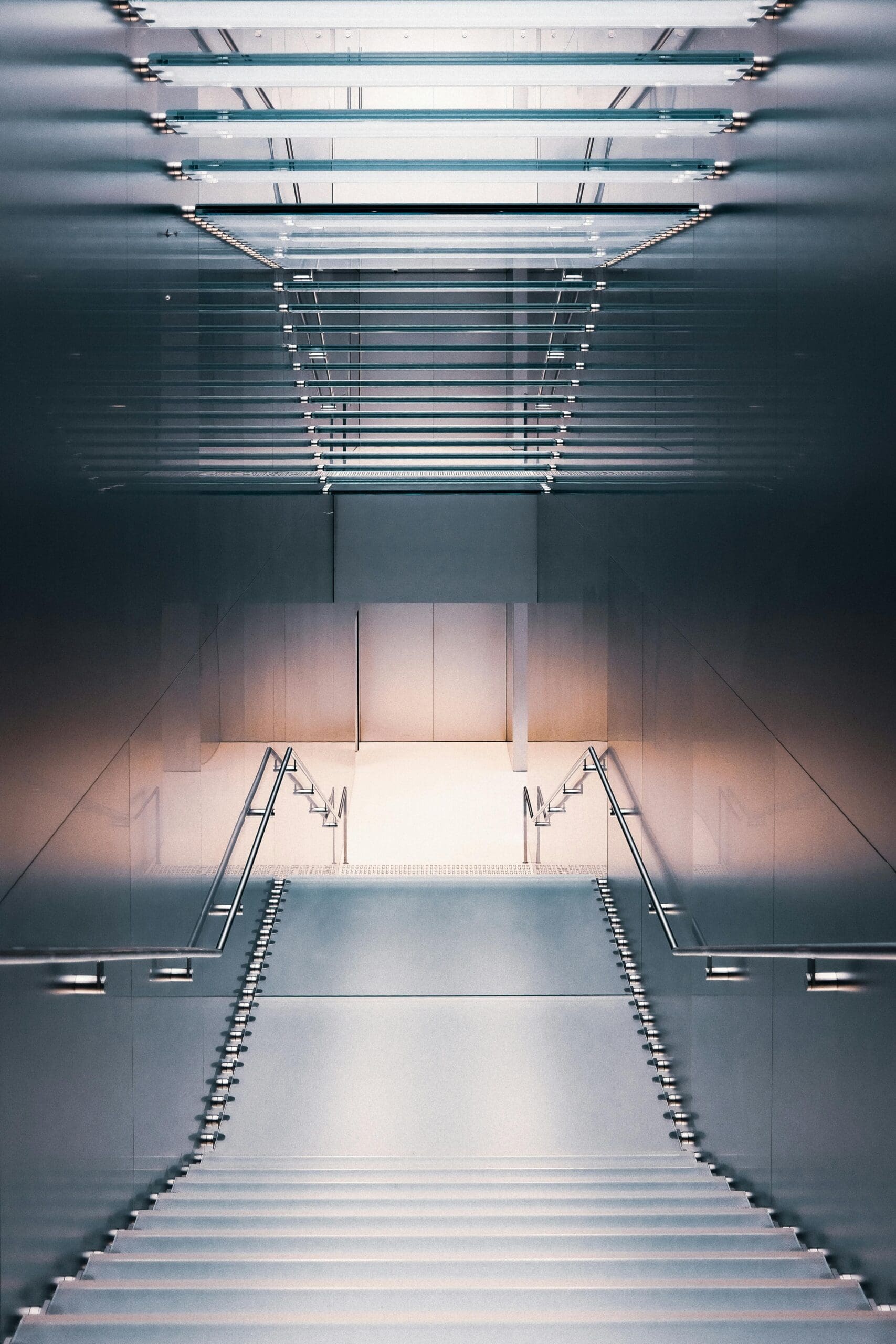 Escalier moderne et élégant menant vers le bas dans un espace architectural minimaliste. Les marches sont flanquées de rampes métalliques et éclairées par un éclairage d'ambiance doux depuis le haut et le bas, créant une apparence symétrique et futuriste.
