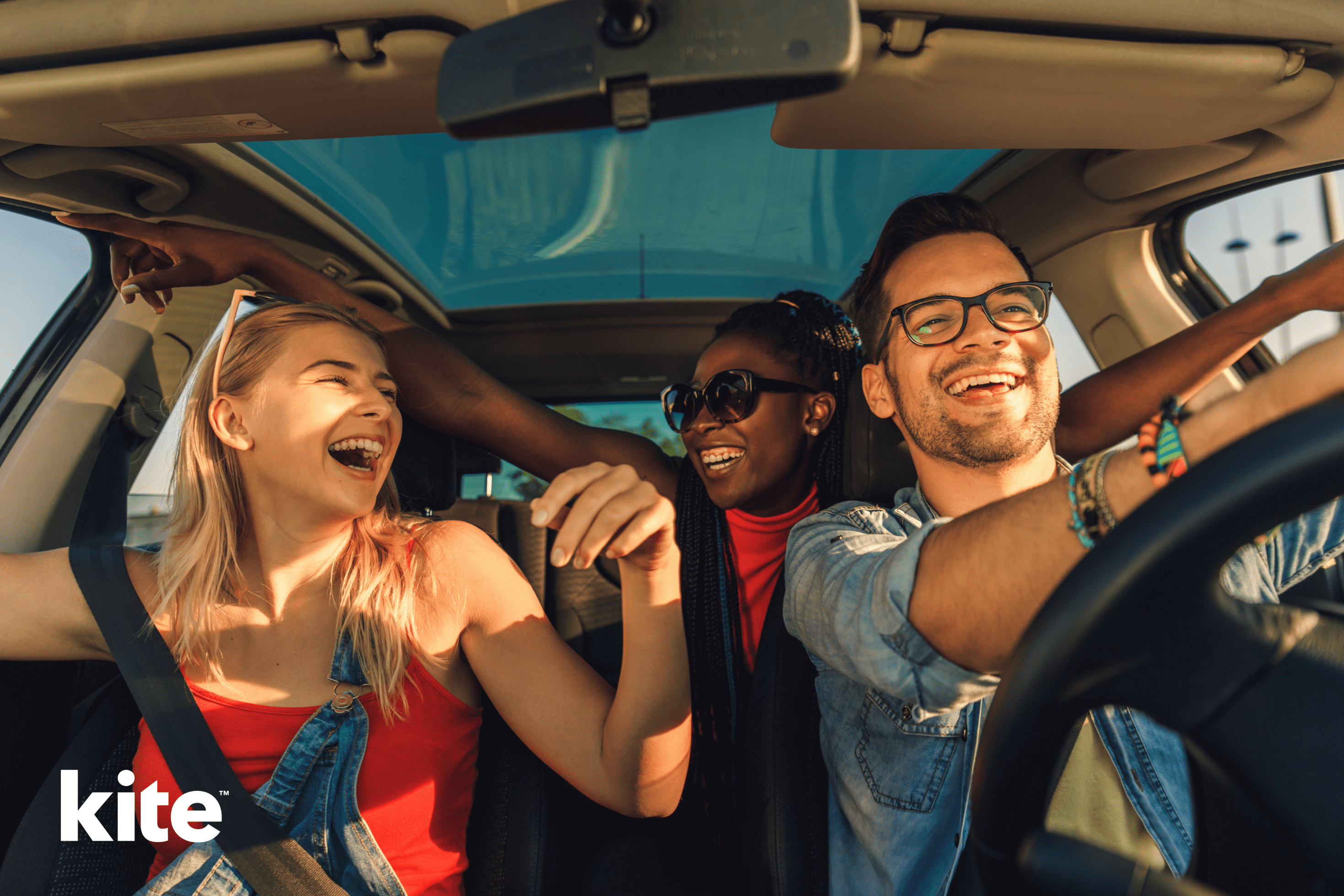 Trois amis sourient et rient à l'intérieur d'une voiture dont le toit ouvrant est ouvert. Une femme portant des lunettes de soleil est assise au milieu du siège arrière. L'homme qui conduit porte des lunettes et un jean, et une femme vêtue d'un haut rouge est assise sur le siège passager avant. Le mot « cerf-volant » se trouve dans le coin.