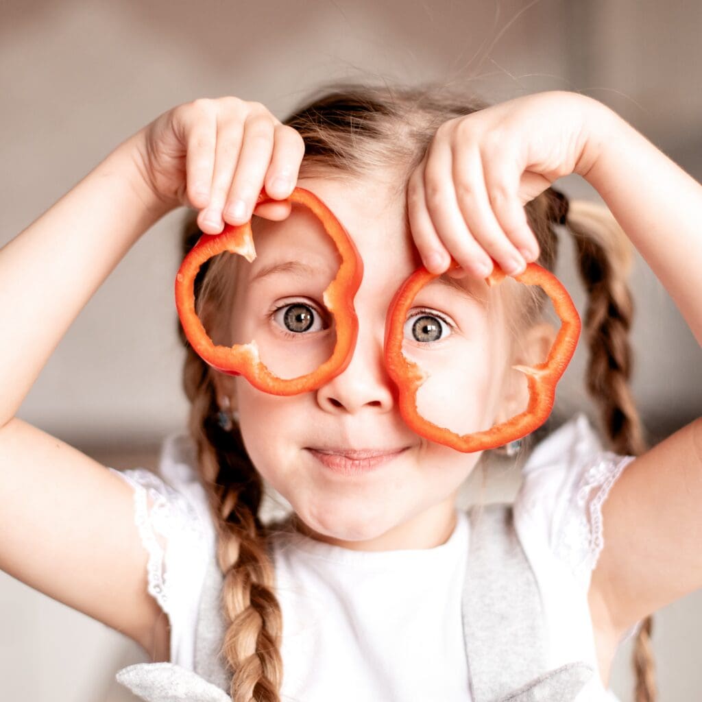 Une enfant tient des poivrons devant son visage